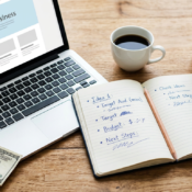 How to start a business with $100 — a workspace flat lay showing a laptop, business plan notebook, and a hundred dollar bill on a wooden desk